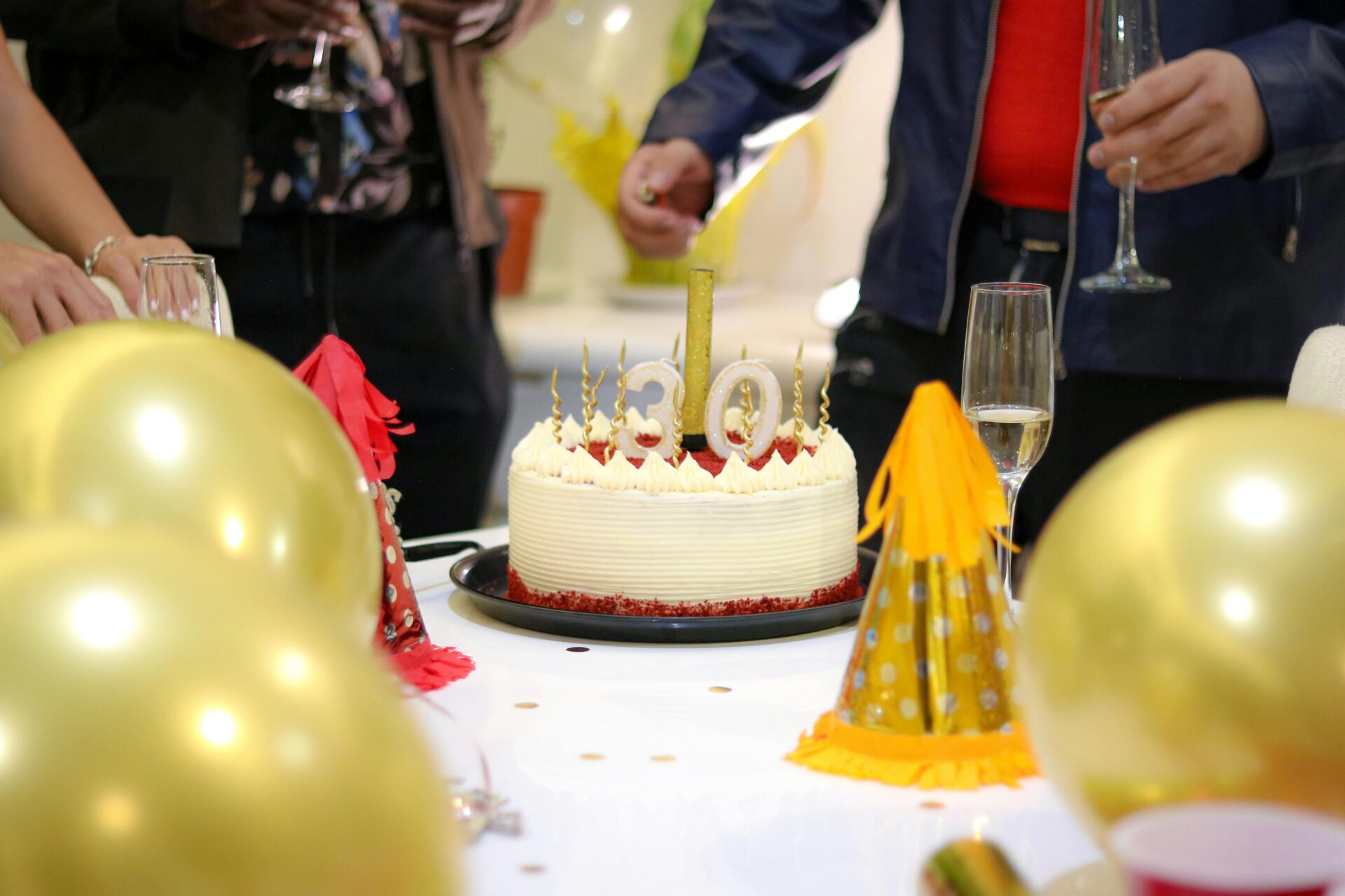 Elegante Geburtstagspartyszene mit einem Red-Velvet-Kuchen, goldenen Luftballons und Partyhüten.