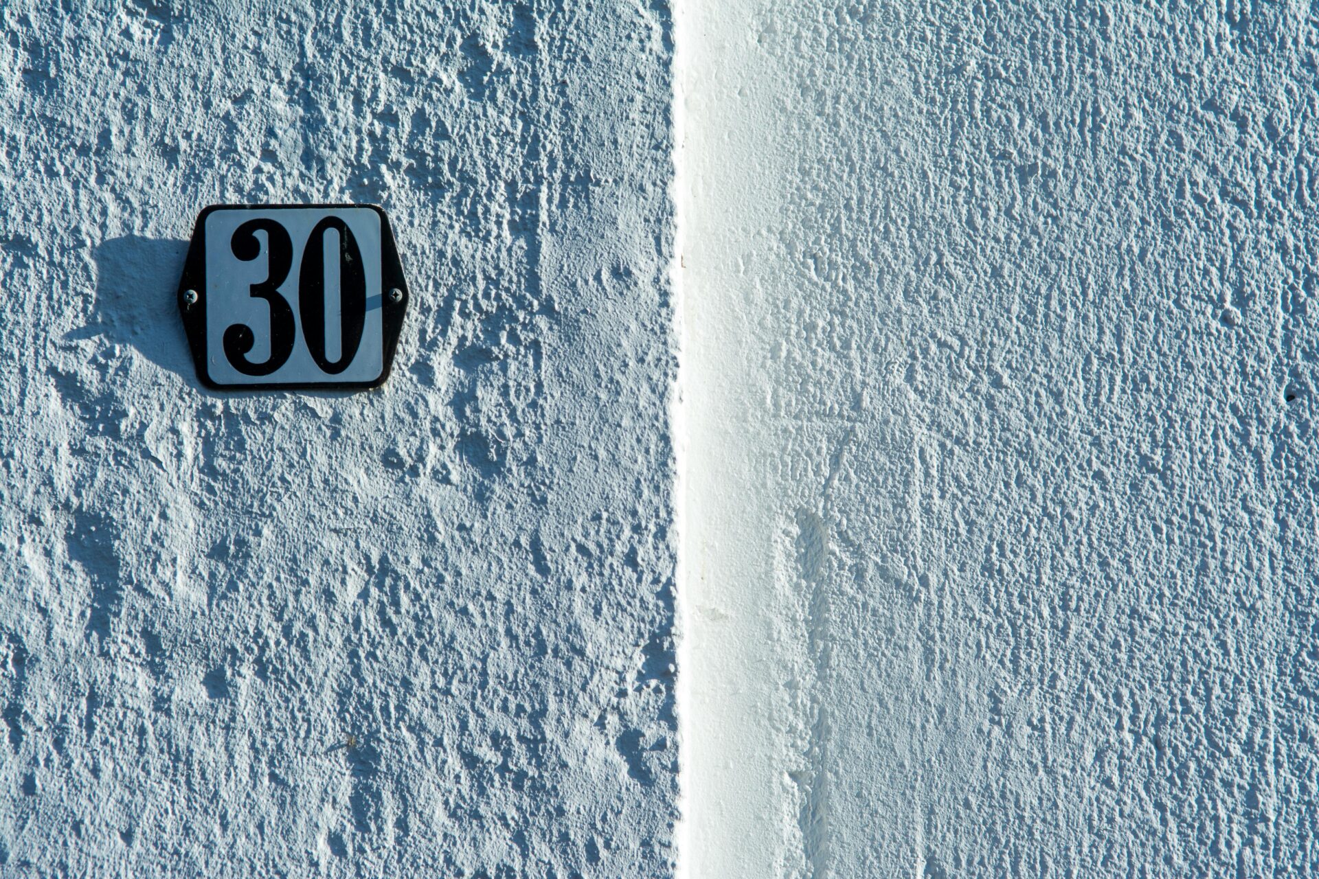 Nahaufnahme einer strukturierten weißen Wand mit einem klassischen Schild mit der Hausnummer 30.