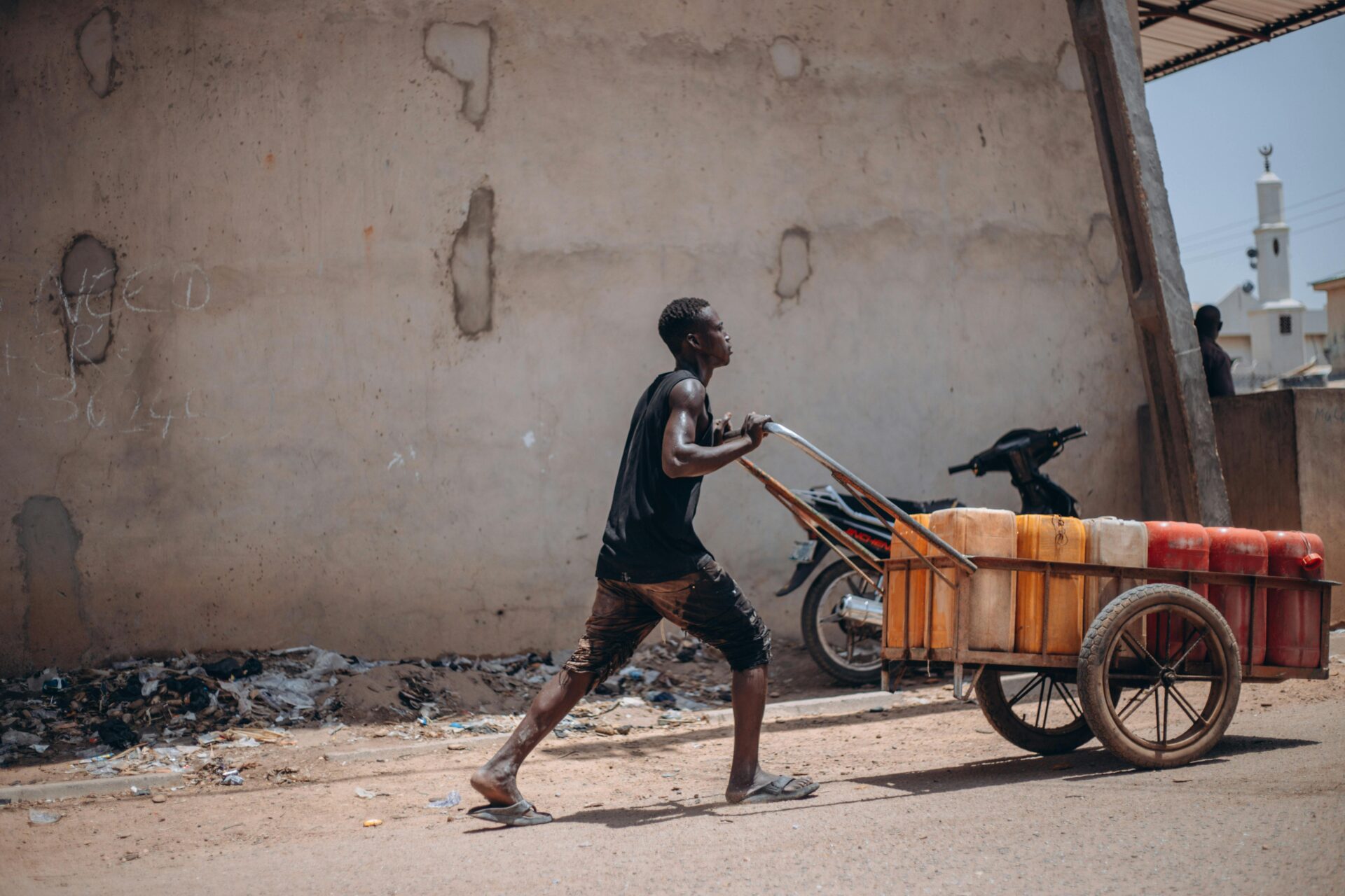Ein junger Mann schiebt einen mit Containern gefüllten Karren eine Straße entlang und zeigt so das tägliche Leben in der Stadt.