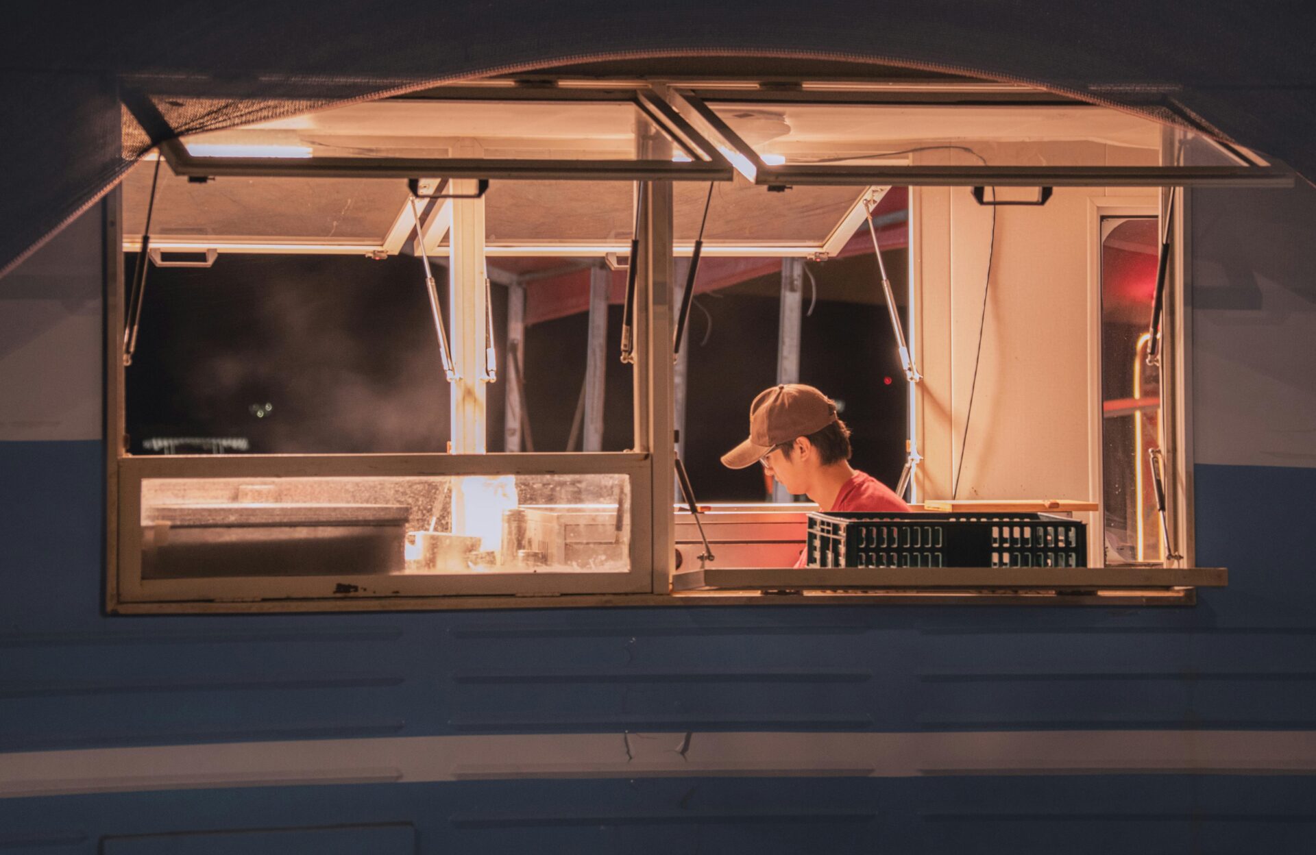 Ein Blick auf einen Arbeiter in einem Imbisswagen bei Nacht, aufgenommen durch ein offenes Fenster.