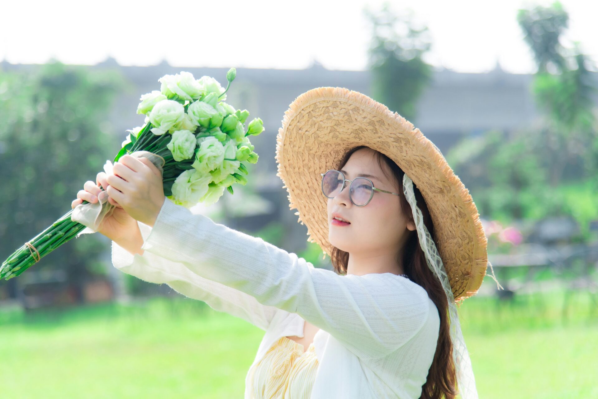L&Atilde;&curren;chelnde Frau mit Sonnenbrille h&Atilde;&curren;lt Blumenstrau&Atilde;Ÿ im sonnigen Park und dr&Atilde;&frac14;ckt ihre Freude am Sommer aus.