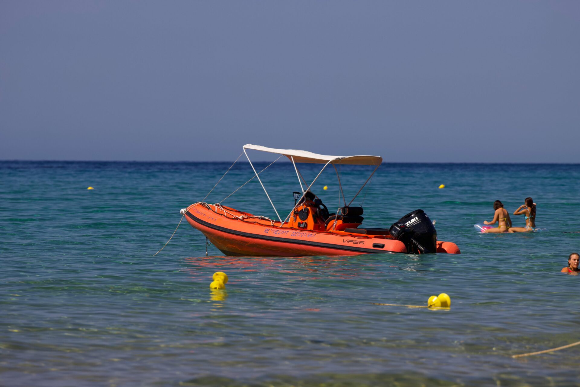 Ein Schlauchboot am Strand von Glyfada auf Korfu, mit Schwimmern, die unter klarem Himmel das azurblaue Ionische Meer genießen.