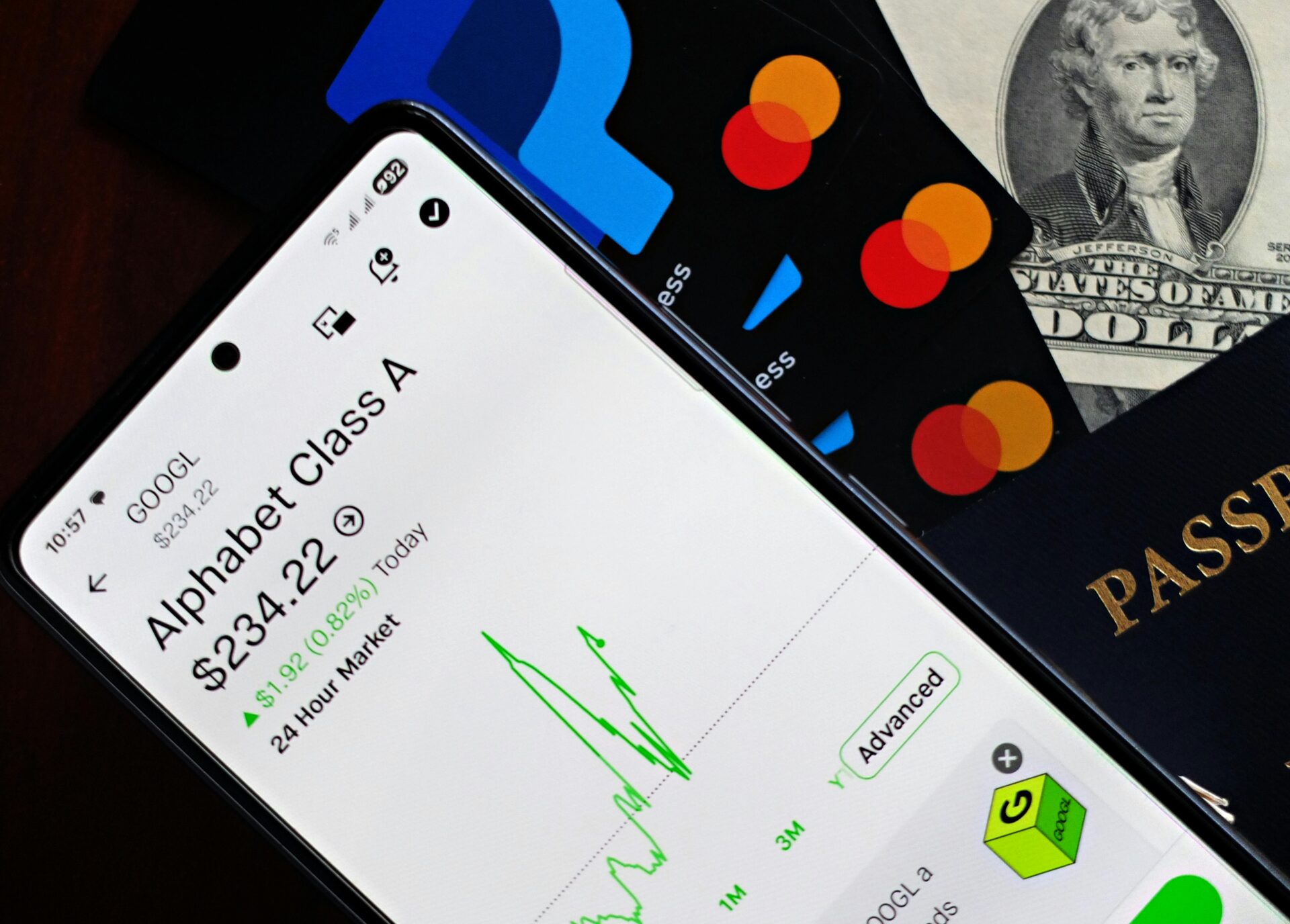 Ein Smartphone, das den Aktienkurs von Alphabet neben Kreditkarten, Bargeld und Reisepass anzeigt.