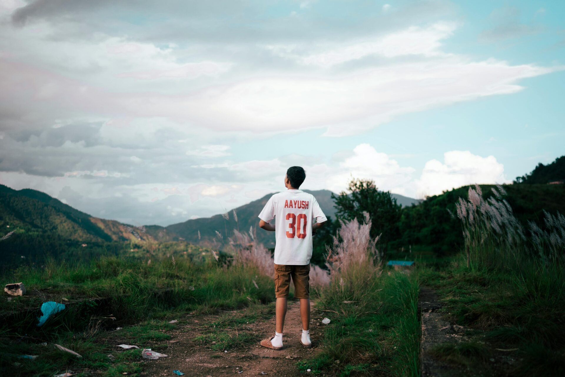 Ein kleiner Junge steht auf einem Hügel mit malerischem Bergblick und trägt ein weißes Trikot mit der Nummer „30“ auf dem Rücken.