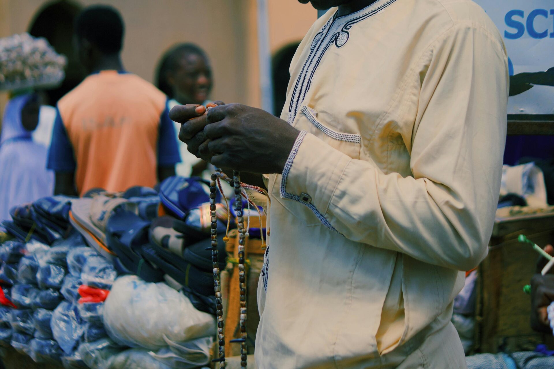 Ein Mann in traditioneller Kleidung verkauft Perlen auf einem lebhaften Markt im Freien in Nigeria.